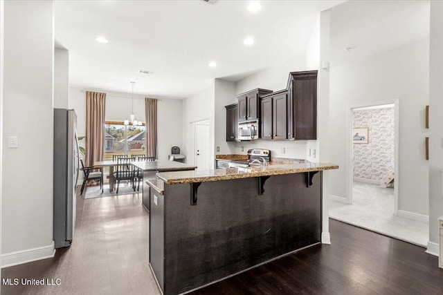 kitchen featuring kitchen peninsula, a breakfast bar area, stainless steel appliances, dark hardwood / wood-style flooring, and light stone counters