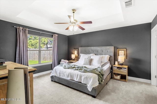 bedroom with ceiling fan, light colored carpet, and a tray ceiling