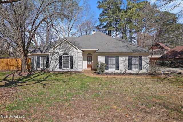 view of front facade featuring brick siding, a chimney, a front yard, and fence