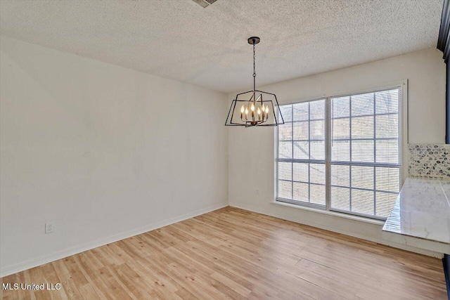 unfurnished room featuring light wood-style flooring, a notable chandelier, baseboards, and a textured ceiling