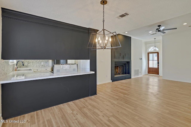 kitchen featuring dark cabinetry, visible vents, light wood finished floors, a fireplace, and a sink