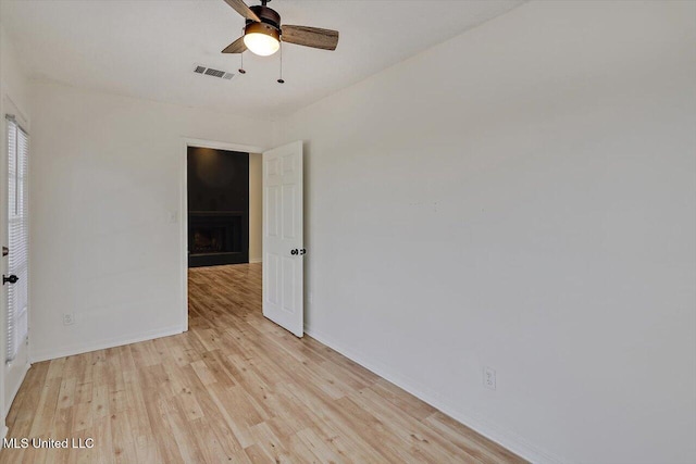 unfurnished room with visible vents, baseboards, ceiling fan, light wood-type flooring, and a fireplace