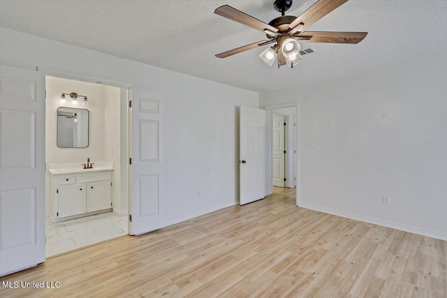 unfurnished bedroom with a sink, light wood-type flooring, ensuite bathroom, and a textured ceiling