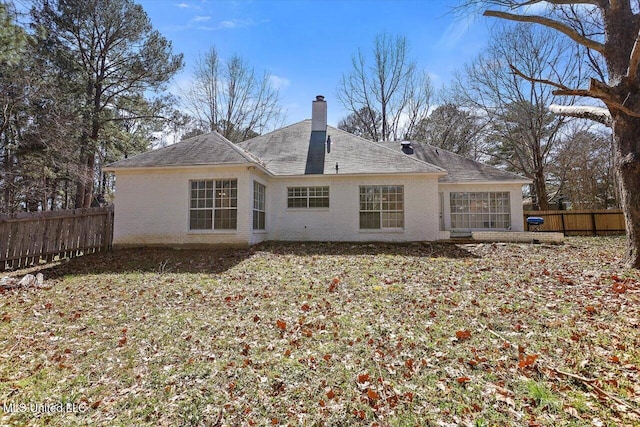 rear view of property featuring brick siding, a chimney, and fence