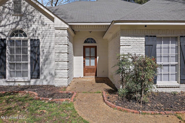 view of exterior entry with brick siding and a shingled roof