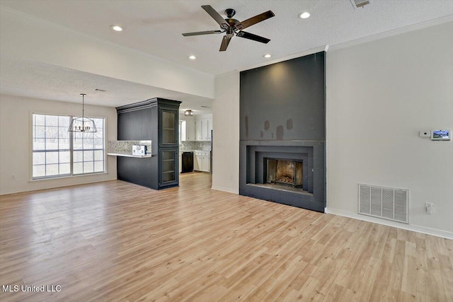 unfurnished living room featuring visible vents, ornamental molding, light wood-style floors, ceiling fan with notable chandelier, and a large fireplace