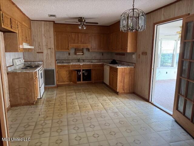 kitchen with wooden walls, brown cabinetry, under cabinet range hood, and white appliances