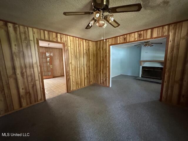 unfurnished living room featuring wooden walls, a fireplace, carpet floors, a textured ceiling, and a ceiling fan