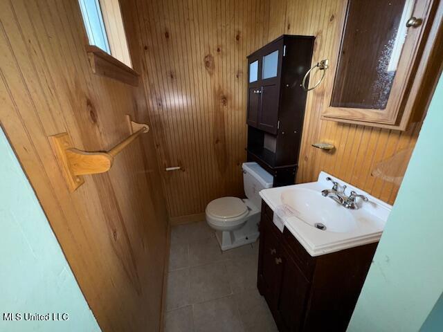 half bath with vanity, tile patterned floors, wooden walls, and toilet
