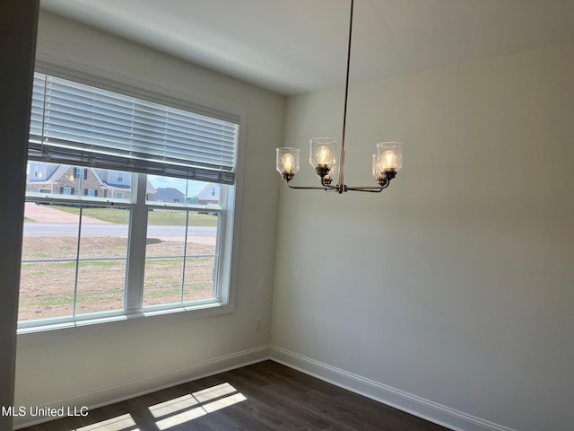 unfurnished dining area with a chandelier, baseboards, and dark wood-style flooring