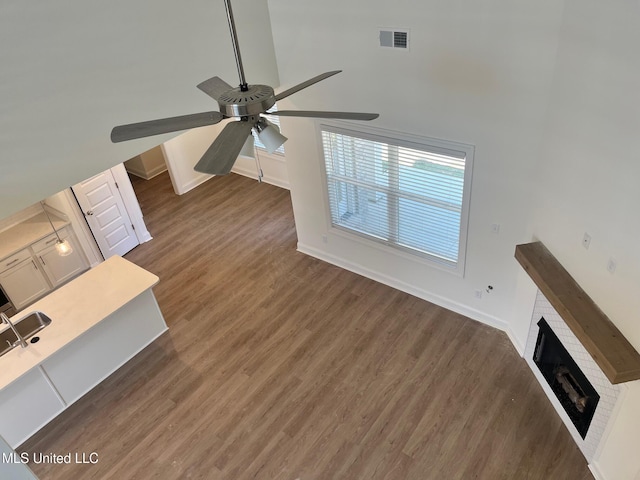 unfurnished living room with ceiling fan, wood finished floors, a brick fireplace, baseboards, and a towering ceiling