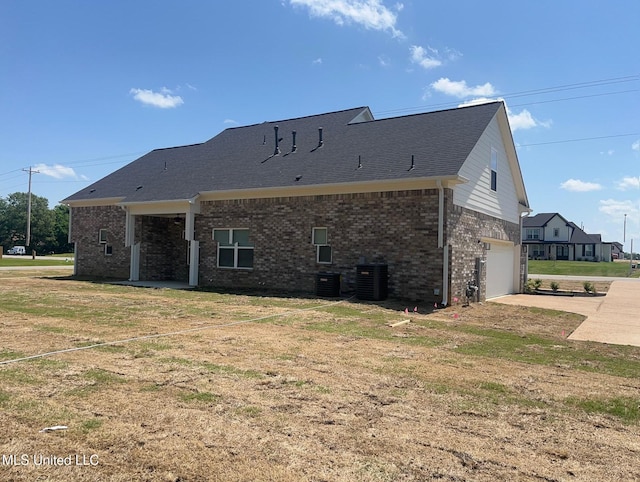 back of house with brick siding, central AC unit, an attached garage, and driveway