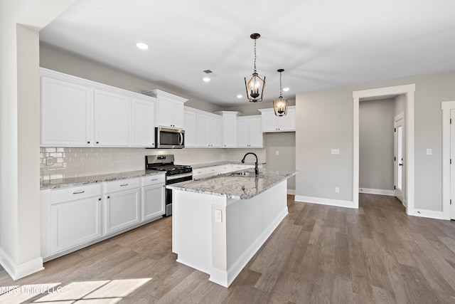 kitchen with light stone counters, decorative light fixtures, a center island with sink, white cabinets, and appliances with stainless steel finishes