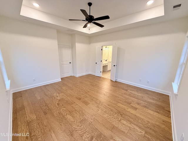 empty room featuring a raised ceiling, ceiling fan, and light wood-type flooring