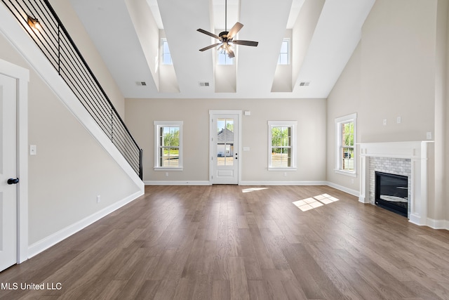 unfurnished living room featuring ceiling fan, a fireplace, a towering ceiling, and hardwood / wood-style floors