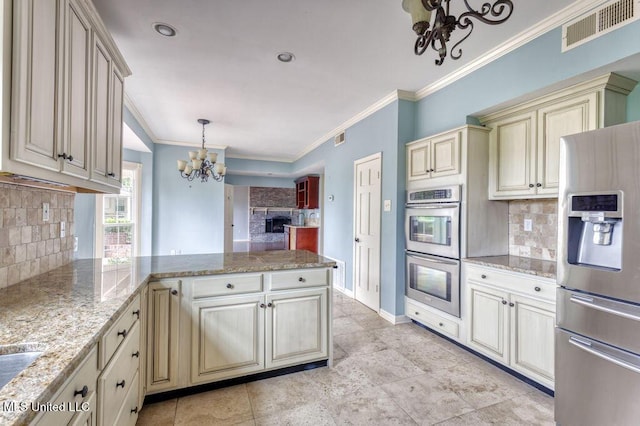 kitchen featuring cream cabinets, decorative light fixtures, backsplash, stainless steel appliances, and light stone countertops