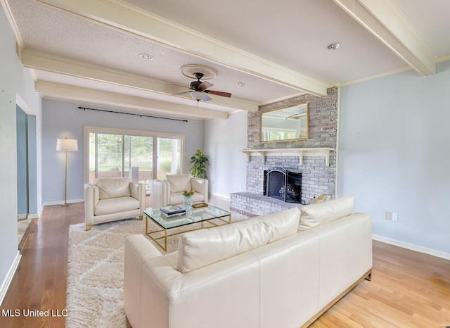 living room featuring crown molding, hardwood / wood-style flooring, ceiling fan, a fireplace, and beamed ceiling