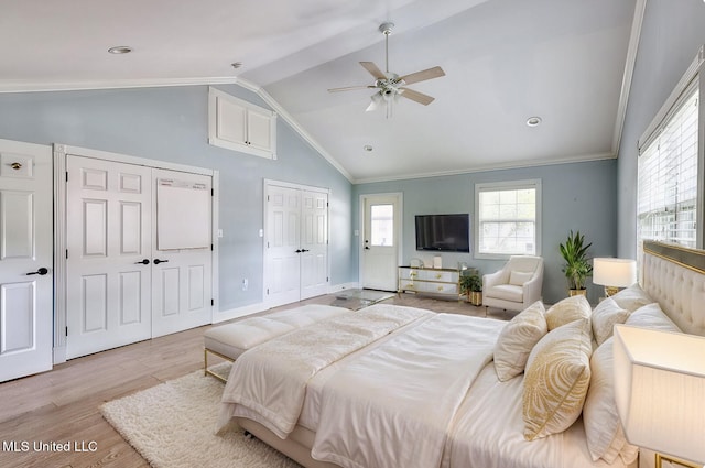 bedroom featuring vaulted ceiling, light hardwood / wood-style flooring, ornamental molding, two closets, and ceiling fan