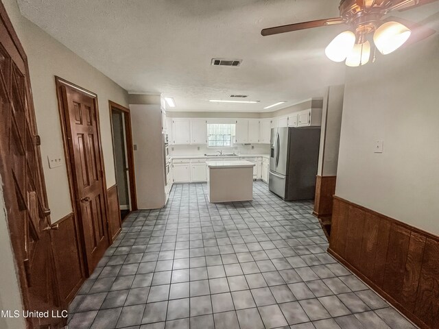 kitchen with a textured ceiling, a center island, stainless steel fridge, ceiling fan, and white cabinets