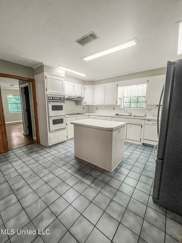 kitchen featuring white cabinets, a center island, a wealth of natural light, and white appliances