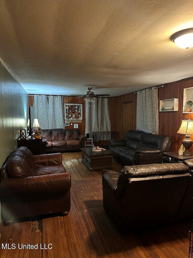 living room with dark wood-type flooring, ceiling fan, a textured ceiling, and wooden walls