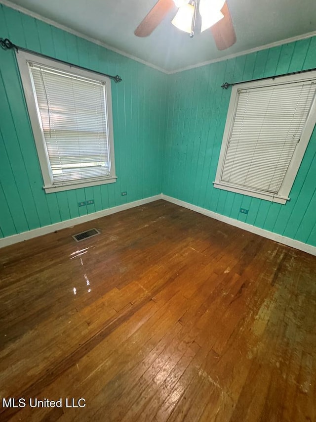 unfurnished room featuring hardwood / wood-style floors, wood walls, ceiling fan, and crown molding