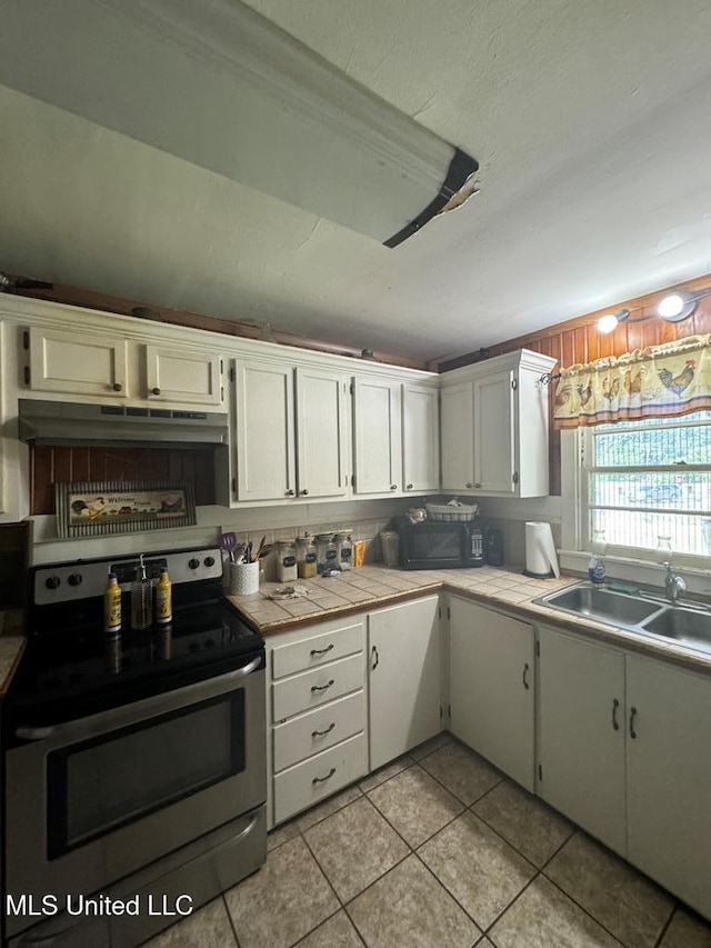 kitchen featuring light tile patterned flooring, white cabinetry, sink, stainless steel range with electric cooktop, and tile counters