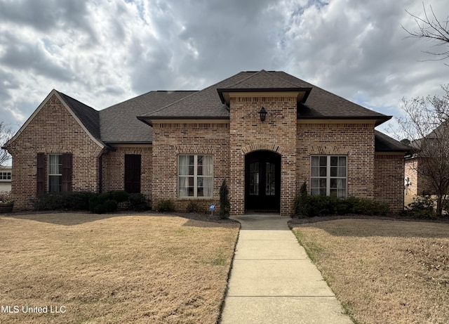 french country inspired facade featuring brick siding, a shingled roof, and a front lawn