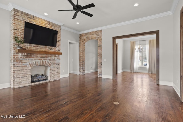 unfurnished living room featuring wood finished floors, baseboards, crown molding, a brick fireplace, and ceiling fan with notable chandelier