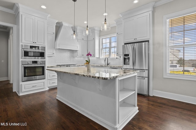 kitchen with custom range hood, white cabinets, appliances with stainless steel finishes, backsplash, and a center island