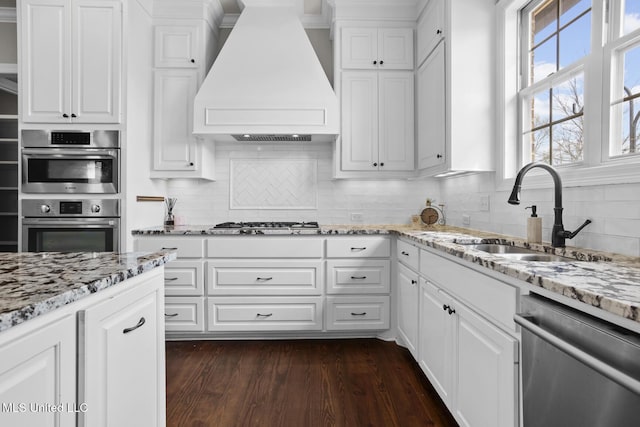 kitchen with a sink, custom exhaust hood, appliances with stainless steel finishes, and white cabinetry