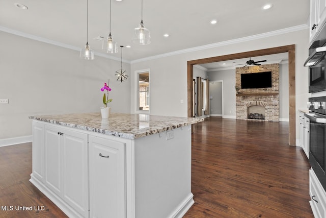 kitchen with a ceiling fan, a kitchen island, dark wood finished floors, white cabinetry, and a fireplace