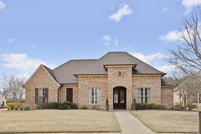 french provincial home with a front yard, brick siding, and a shingled roof