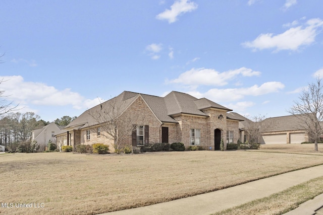 french country home featuring brick siding, driveway, and a front lawn