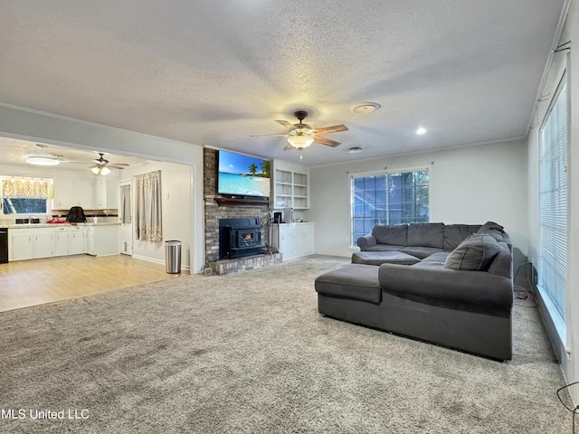 living room with a textured ceiling, ceiling fan, crown molding, light hardwood / wood-style flooring, and a wood stove