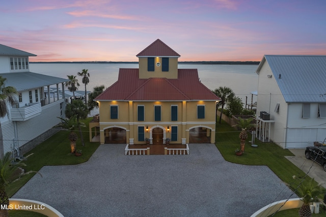 view of front of home with stucco siding, a water view, gravel driveway, a patio area, and metal roof