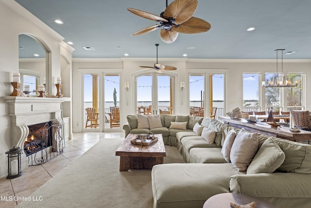 living room featuring ornamental molding, light tile patterned floors, a fireplace with flush hearth, a ceiling fan, and a water view