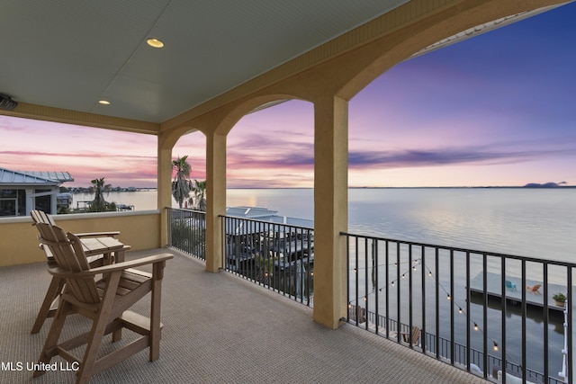 balcony at dusk featuring a water view