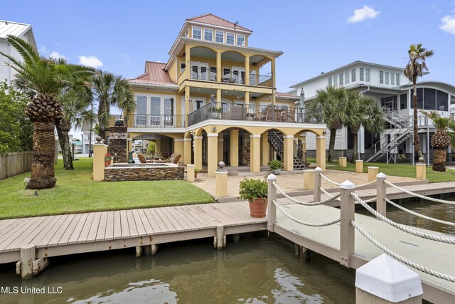 rear view of property featuring stairway, a balcony, a lawn, and a water view