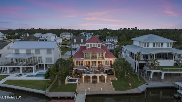 back of property at dusk with a balcony, a patio area, stairway, metal roof, and a lawn