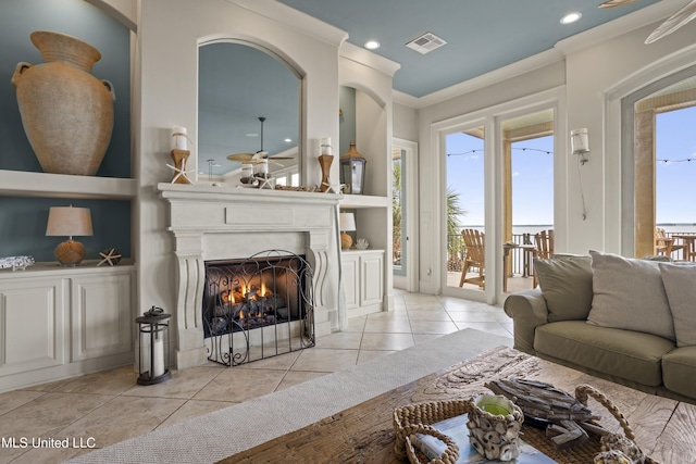 living room featuring ceiling fan, light tile patterned floors, ornamental molding, recessed lighting, and a fireplace with flush hearth