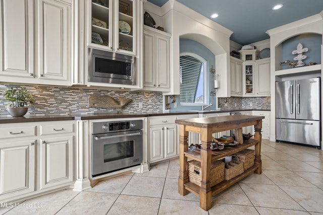 kitchen featuring appliances with stainless steel finishes, dark countertops, light tile patterned flooring, backsplash, and recessed lighting