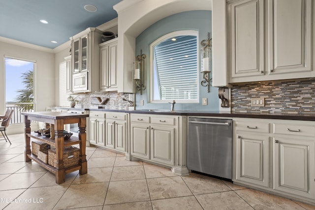 kitchen featuring appliances with stainless steel finishes, a sink, decorative backsplash, light tile patterned flooring, and dark countertops