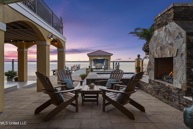 view of patio featuring an outdoor stone fireplace, a water view, and a balcony