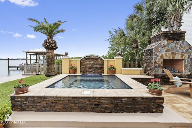 view of pool featuring an outdoor stone fireplace, a jacuzzi, a water view, and fence