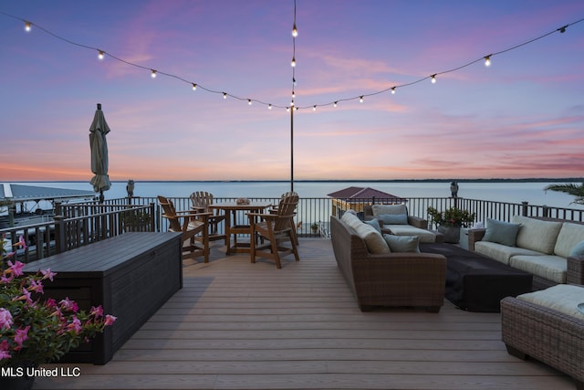 deck at dusk with outdoor lounge area and a water view