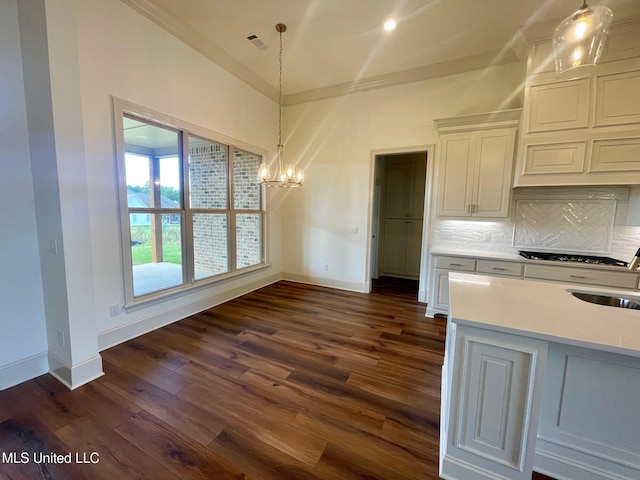 kitchen with dark hardwood / wood-style flooring, backsplash, crown molding, white cabinets, and hanging light fixtures