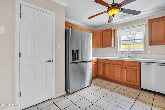 kitchen with tile countertops, light tile patterned floors, stainless steel appliances, ornamental molding, and a sink