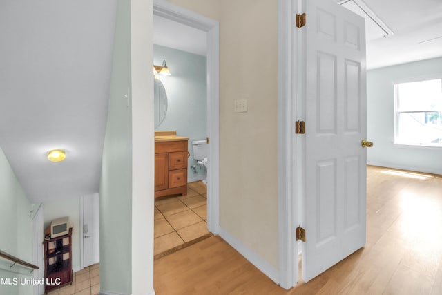 hallway featuring attic access, baseboards, and light wood finished floors