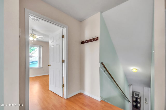 corridor with baseboards, an upstairs landing, visible vents, and light wood-style floors